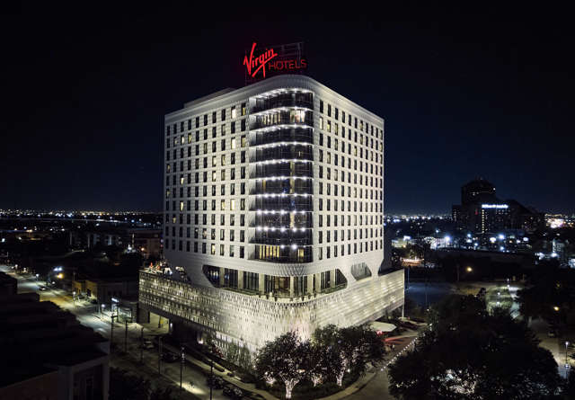 Exterior of Virgin Hotels Dallas at night, illuminated with vibrant lighting.