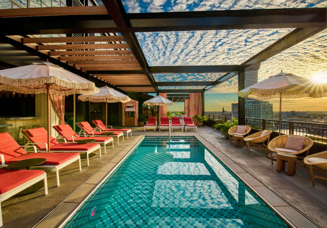 Vibrant rooftop pool club at Virgin Hotels New Orleans with comfortable lounge chairs, a pool, and panoramic city views.
